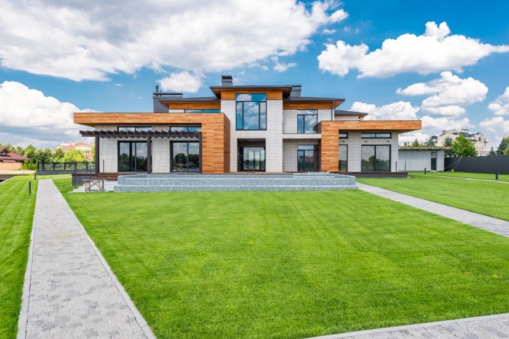 Exterior of contemporary residential house with glass doors and panoramic windows near green lawn with paved paths on sunny day in summer